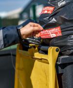 Une personne appose un autocollant refus de collecte sur un bac jaune