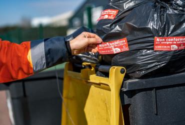 Une personne appose un autocollant refus de collecte sur un bac jaune